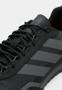 Μαύρα αθλητικά παπούτσια με υφή υφάσματος και λαστιχένια σόλα, με κορδόνια σε τόνο και τρεις ξεχωριστές ματ ρίγες στο πλάι.