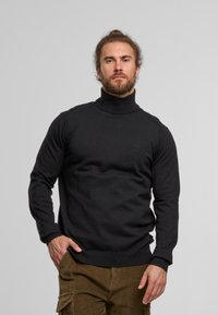 Czarny sweter z golfem, z prążkowanymi detalami oraz dopasowanym krojem, prezentowany na modelce na szarym tle.