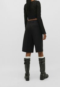 Top de encaje negro de manga larga combinado con pantalones cortos negros de corte ajustado y botas de cuero negro hasta la rodilla con hebillas de metal y suelas gruesas.