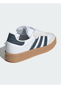 Fehér sneaker tengerészkék csíkokkal, velúr kiegészítőkkel és bézs gumitalppal. Párnázott nyakkal és texturált talppal rendelkezik a jobb tapadás érdekében.