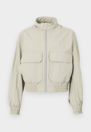 Lys grå cropped jakke med høj krave, frontlynlås og to store brystlommer. Elastiske manchetter og kant tilføjer struktur.