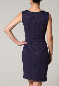 Námořnicky modré krajkované šaty s přiléhavým siluetou, bez rukávů a texturovaným květinovým vzorem. Zapínání na zadním zipu a hladký saténový lem.