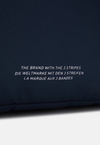 Sjöblått tyg med en strukturerad yta, med vit text på flera språk: "Märket med de 3 ränderna" och relaterade fraser.
