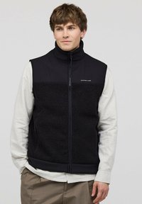 Schwarze Fleece-Weste mit glattem Oberteil und strukturiertem Unterteil, hohem Kragen und seitlichen Reißverschlusstaschen. Logo auf der Brust.