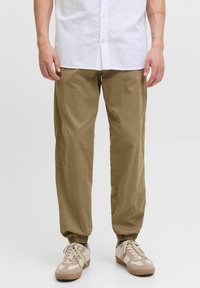 Pantalons de jogging kaki avec poignets élastiques, en tissu léger. Associés à des baskets de teinte neutre et à une chemise blanche à boutons.