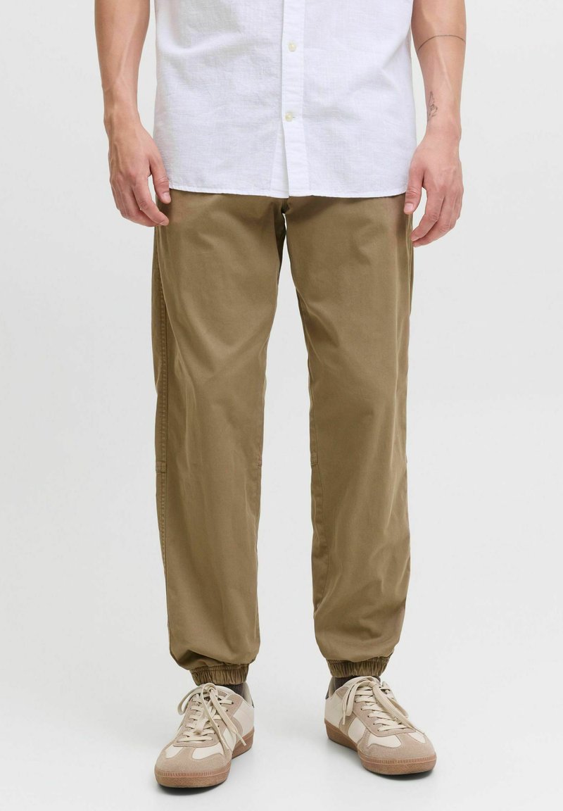 Pantalons de jogging kaki avec poignets élastiques, en tissu léger. Associés à des baskets de teinte neutre et à une chemise blanche à boutons.