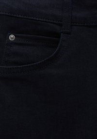 Gros plan sur un tissu denim foncé mettant en avant une poche avant avec des coutures détaillées et un petit rivet métallique.
