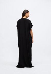 Fekete maxiruha puha anyagból, rövid ujjakkal, bő fazonnal és hosszú, áramló kialakítással, látható rögzítők nélkül.