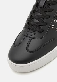 Basket en cuir noir avec une finition lisse, bout arrondi, semelle épaisse blanche et lacets noirs avec œillets en métal pour une durabilité accrue.
