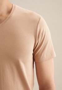 T-shirt V en beige clair en coton doux, avec des manches courtes et une surface lisse, sans texture.