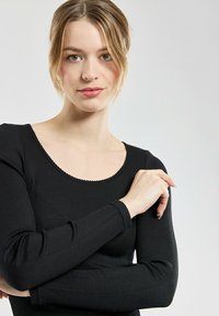 Haut noir àrayures côtelées à manches longues, avec un col rond et un empiècement festonné, doté de manches ajustées et d'une surface texturée.