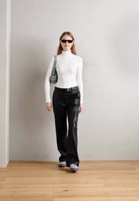 Un turtleneck blanc ajusté, un pantalon noir à jambes larges, des chaussures bleu clair et un petit sac bandoulière gris. Des textures fluides dans une tenue décontractée.