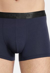 Navy blue boxer briefs made of stretch fabric with a soft, elastic black waistband featuring embossed logo. Fitted design with medium leg length.