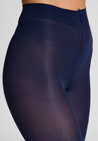 Marineblaue High-Waist-Leggings aus dehnbarem, weichem Material mit glatter Textur und subtiler Ausstrahlung, die ein nahtloses Design aufweisen.