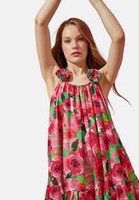 Vestido floral en rosa, con acentos en forma de rosa en los hombros, tela fruncida y un dobladillo con volantes. El material parece ligero y etéreo.