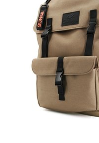 Sac à dos en toile beige avec quincaillerie et accents noirs. Il comporte une poche à rabat à l'avant et une étiquette affichant "SUN68" en orange vif.
