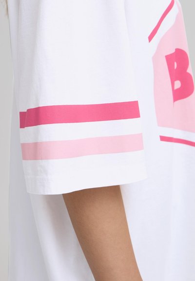 Camiseta blanca de algodón con acentos a rayas rosas en las mangas y un diseño impreso audaz. Textura suave con un corte relajado.