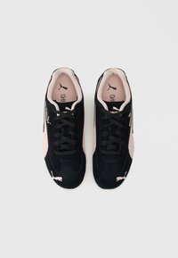 Črne suede superge z roza detajli, zvesto zasnovane s vezalkami, oblazinjeno ovratnikom in teksturiranimi podplati. Puma logo na straneh in na jeziku.