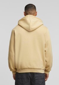 Beige hoodie met een trekkoordcapuchon, ribgebreide manchetten en zoom. Soepele textuur, relaxte pasvorm en geen zichtbare patronen of logo's.