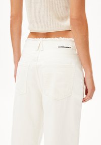 Witte denim jeans met een rafelige taille, twee achterzakken en een "ARMEDANGELS"-label aan de achterkant. Soepele textuur, ontspannen pasvorm.
