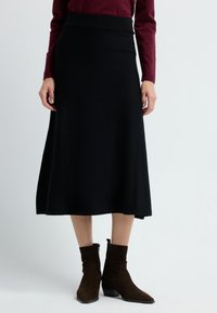 Zwarte A-lijn rok met een geribbeld tailleband, gecombineerd met bruine suède enkelboots met een zijrits en een bescheiden hak.