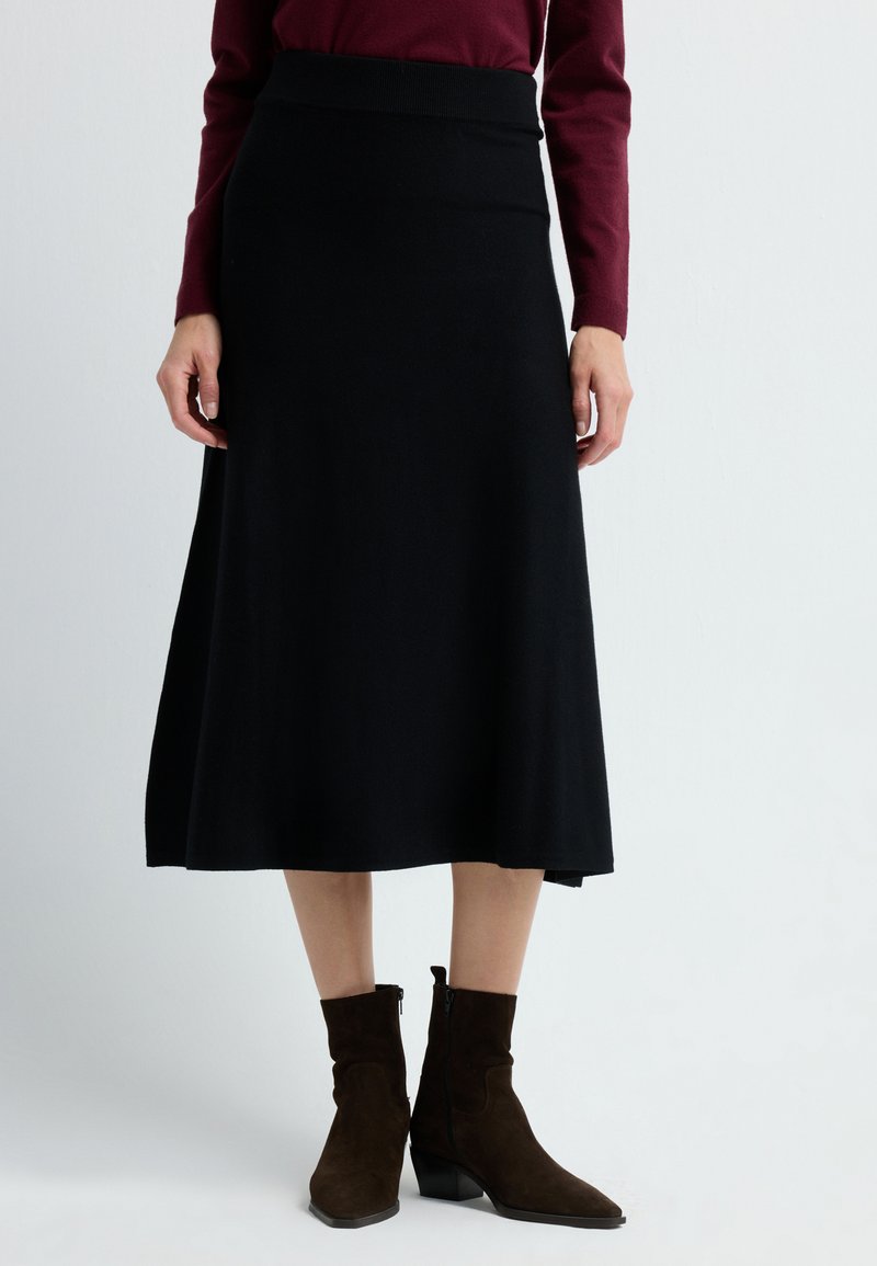 Zwarte A-lijn rok met een geribbeld tailleband, gecombineerd met bruine suède enkelboots met een zijrits en een bescheiden hak.