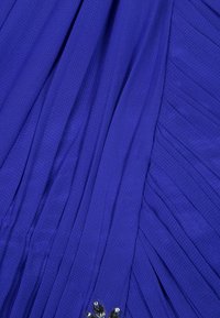 Plisserad klänning i en livlig kunglig blå färg med ett texturerat mönster och en silver blommig detalj nära fållen.