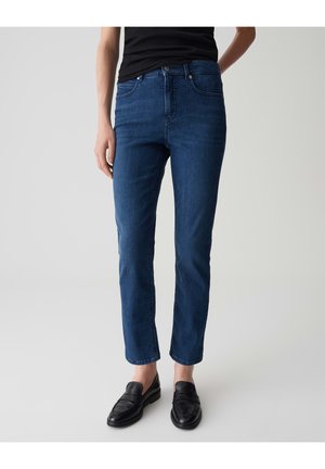 Donkerblauwe denim jeans met een slim fit, voorzien van een klassieke vijf-pocketontwerp en een knoopsluiting. Gecombineerd met zwarte instappers.
