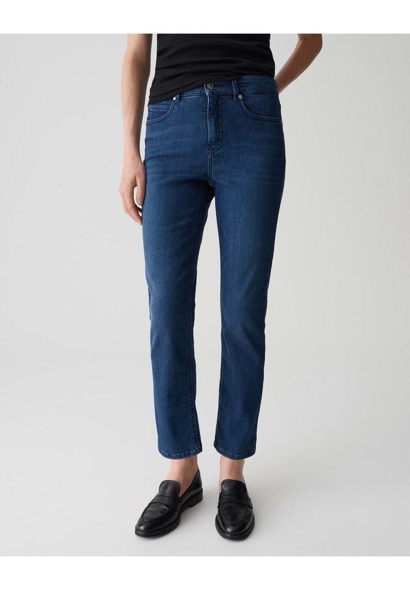 Jeans in denim blu scuro a taglio slim, con un design classico a cinque tasche e chiusura con bottone. Abbinati a mocassini neri.