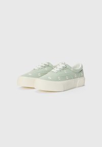 Green canvas sneakers with white daisy embroidery, rounded toe, and white rubber sole and laces. Soft texture with a low-profile design.