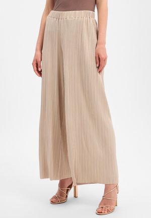 Beige pleated wide-leg pants paired with strappy gold high-heeled sandals on a standing person against a plain background.