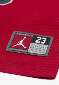 Rode sportstof met een gestikte label waarop het Jumpman-logo, nummer 23 en tekst die kwalitatieve producten prijst geïnspireerd door de beste speler, staan.