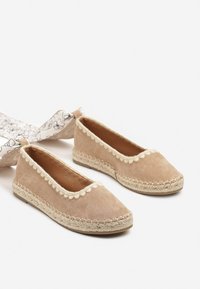 Espadrilles en suède beige avec une semelle plate en jute, présentant des bords ondulés et un design de bout arrondi. Construction simple et légère.