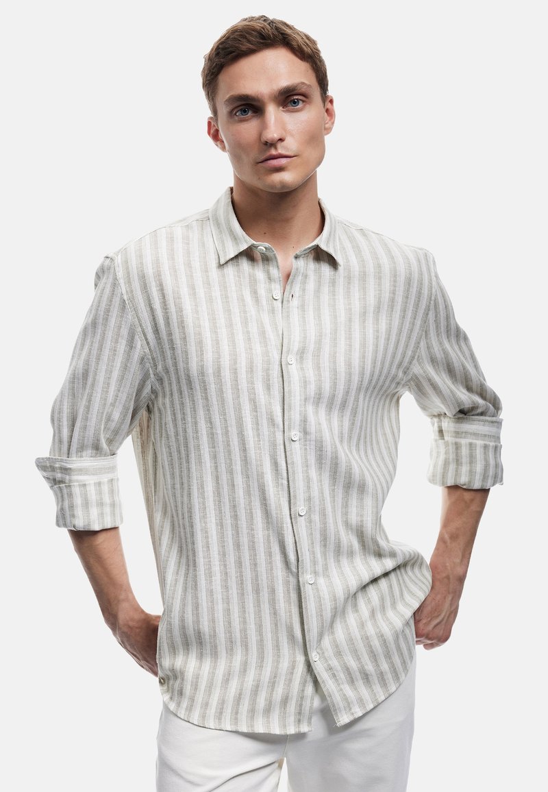 Camisa ligera de lino en color beige con rayas blancas verticales. Cuenta con un frente abotonado, mangas enrolladas y un dobladillo curvado.