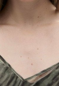 T-shirt vert olive à col en V en tissu lisse, doté d'une bordure en dentelle le long de l'encolure et de légers petits points à la surface.