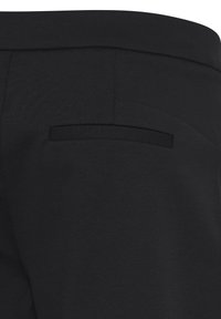Pantalon noir ajusté montrant un gros plan de la ceinture arrière et d'une poche passepoilée simple.