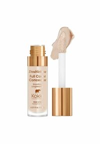 Kokie Professional Doubletime Full Cover Concealer i et klart glasrør med et gyldent låg, ved siden af en beige cremestribe på en hvid applikator.