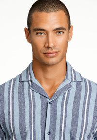 Camicetta a maniche corte a righe con tonalità alternate di blu e bianco, dalla consistenza morbida e colletto piegato, chiusa con bottoni blu.