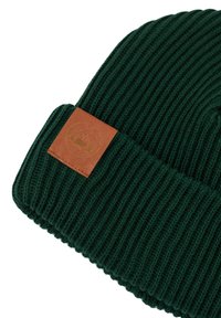 Zielona, prążkowana czapka beanie z brązową skórzaną naszywką z okrągłym wzorem górskim, prezentująca teksturę i zorganizowany design.
