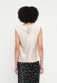 Sateng, ermeløs topp i lys beige med en åpning bak, kombinert med et svart skjørt med hvite polkadotter.