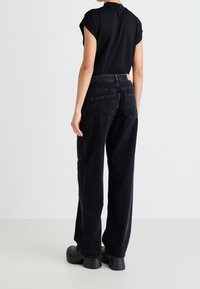 Svart, oversized denimjeans med hög midja, raka ben och två bakfickor, ihop med en åtsittande svart topp och träsandaler.