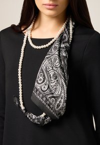 Czarnobiały szal w wzór paisley nałożony na czarny top, zestawiony z naszyjnikiem z pereł. Szal ma misterny wzór i gładką teksturę.