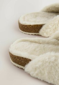 Pantofole in pelliccia sintetica con parte superiore morbida color crema, suola simil sughero e rivestimento interno bianco texturizzato, con design a scivolo.