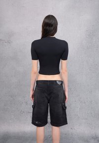 Camisa negra corta de mangas cortas combinada con pantalones cortos cargo negros que cuentan con grandes bolsillos y detalles desgastados. Fondo gris.