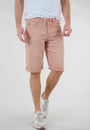 Shorts en denim rose clair avec des ourlets roulés, des poches avant et une petite étiquette sur la taille. Portés avec une chemise blanche et des baskets.