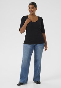 Sort strikket top med V-hals og korte pufærmer, parret med lysblå flare jeans og sorte sko. Glat tekstur og tætsiddende design.