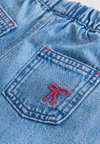 Denim lühikesed püksid, millel on kaks taskut punase õmblusega ja paremalt taskult tikitud dekoratiivne punane lips. Peal elastne vöökoht.
