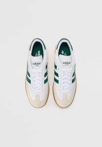Adidas Samba sneakers in white leather with green stripes, a beige rubber toe cap, and gum rubber outsole. Features classic lacing and logo.