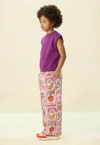 Haut sans manches violet avec un pantalon rose à motifs de fruits et de fleurs. Des baskets avec des accents orange complètent la tenue.