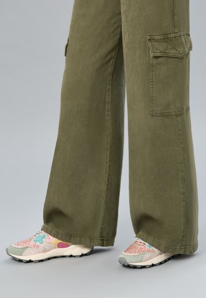 Grüne Cargo-Hose mit weitem Bein, kombiniert mit pastellfarbenen Sneakers mit Blumen- und Sternmustern.